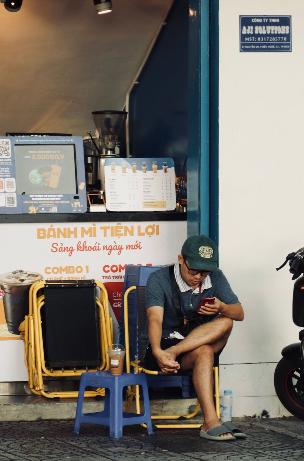Người đàn ông đội mũ ngồi trước quán ăn ở Việt Nam, đang xem điện thoại